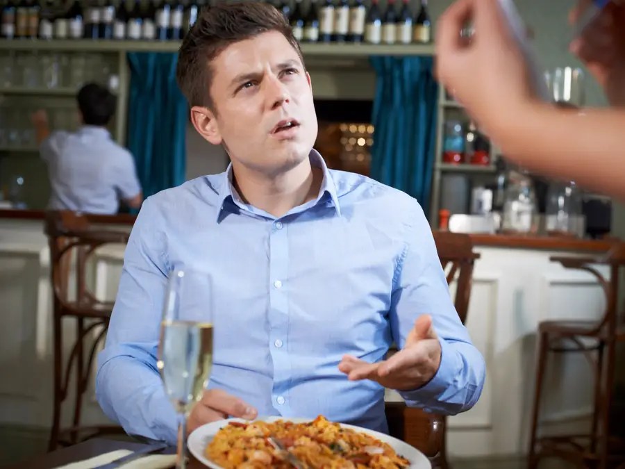 Man in open necked blue shirt complaining about the dish he's been served in a restaurant.