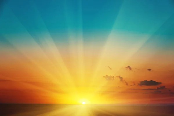 Image of the sun rising on the horizon above the sea, shining out a yellow glow with sun rays, and leaving a clear blue sky above where the rays have yet to reach.
